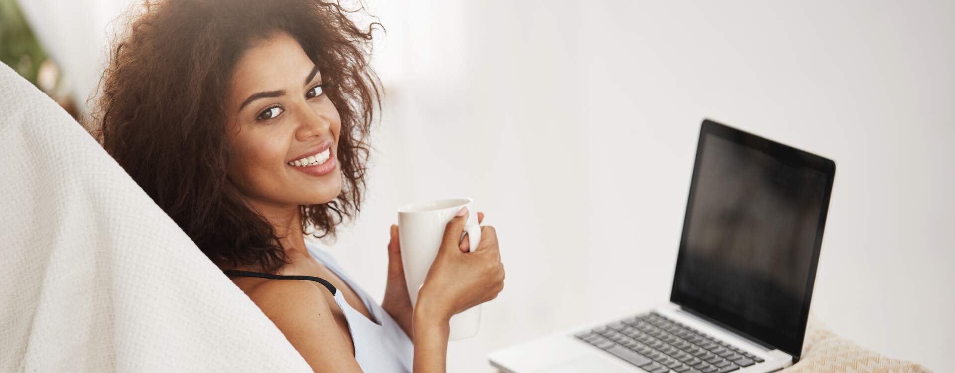 beautiful-african-woman-sleepwear-smiling-holding-cup-sitting-with-laptop-chair-home-alone.jpg